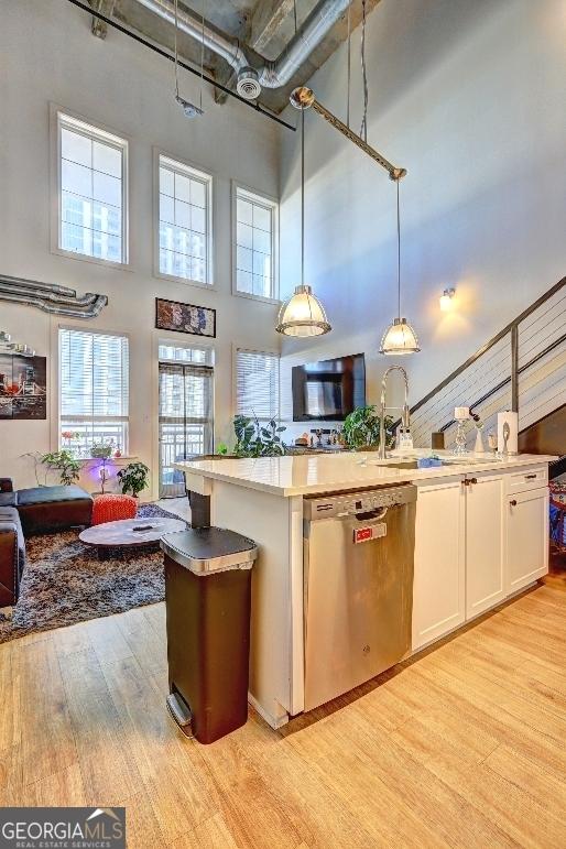 kitchen with open floor plan, light wood-style flooring, stainless steel dishwasher, white cabinetry, and a sink