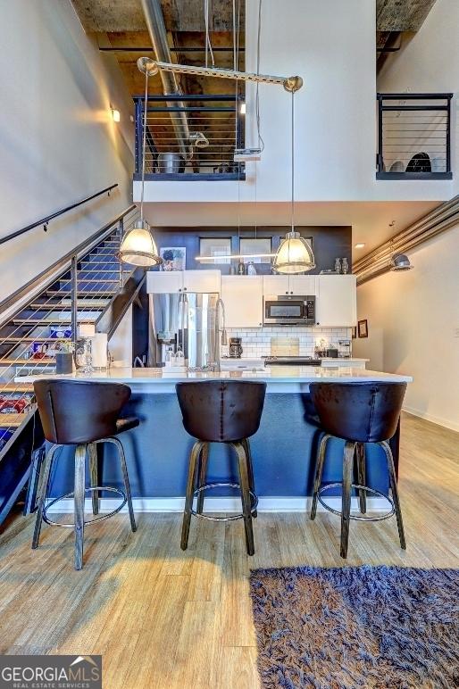 bar featuring light wood-type flooring, a high ceiling, stainless steel appliances, hanging light fixtures, and tasteful backsplash