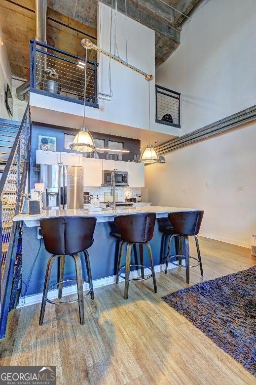 kitchen with hanging light fixtures, a towering ceiling, light wood-style floors, and appliances with stainless steel finishes