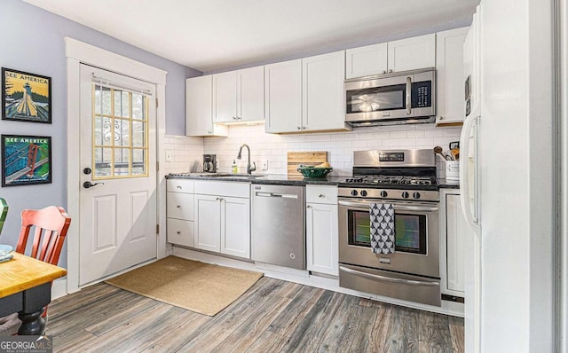 kitchen with appliances with stainless steel finishes, white cabinets, a sink, and wood finished floors
