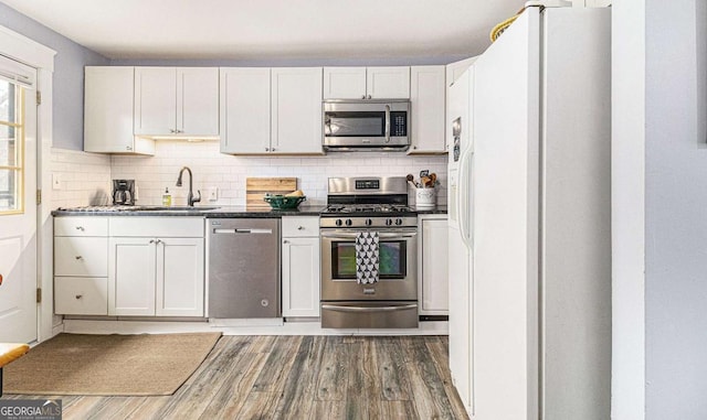 kitchen with stainless steel appliances, tasteful backsplash, white cabinetry, a sink, and wood finished floors