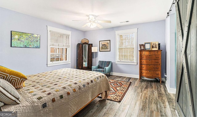 bedroom with visible vents, a barn door, a ceiling fan, wood finished floors, and baseboards