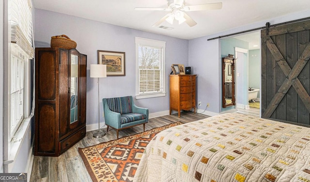 bedroom featuring visible vents, a barn door, a ceiling fan, wood finished floors, and baseboards