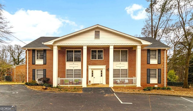 neoclassical / greek revival house with uncovered parking, covered porch, and brick siding