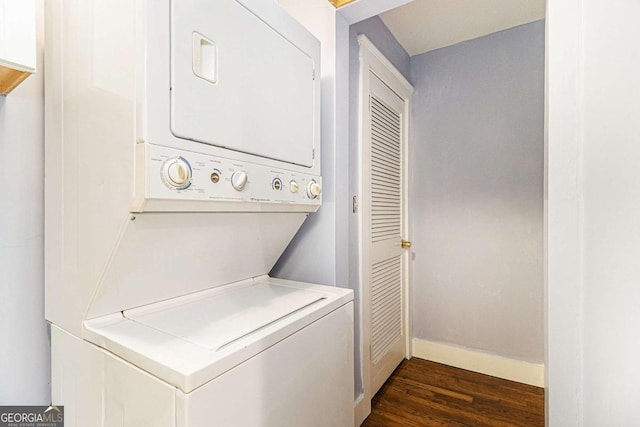 laundry room featuring stacked washer and dryer, laundry area, dark wood-type flooring, and baseboards