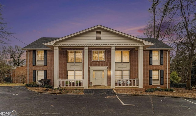 greek revival inspired property featuring covered porch, uncovered parking, and brick siding