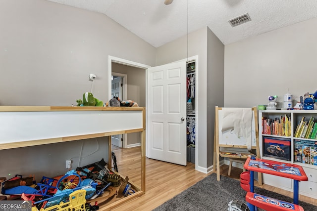 rec room featuring lofted ceiling, a textured ceiling, wood finished floors, and visible vents