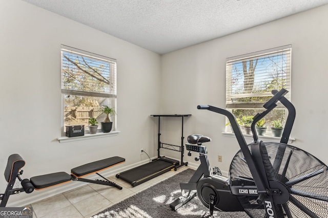 workout area with a textured ceiling, tile patterned flooring, a wealth of natural light, and baseboards