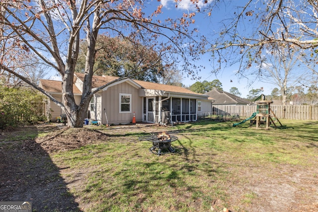 back of property featuring a playground, a lawn, a sunroom, fence, and a fire pit