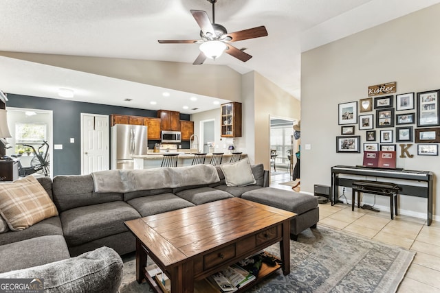 living room with a ceiling fan, lofted ceiling, baseboards, and light tile patterned floors