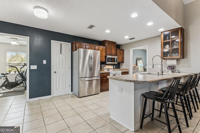 kitchen featuring stainless steel appliances, a peninsula, a sink, visible vents, and glass insert cabinets