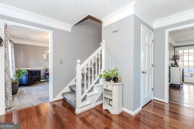 stairway with a textured ceiling, ornamental molding, wood-type flooring, and baseboards