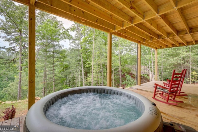 view of patio / terrace with a wooded view, an outdoor hot tub, and a deck