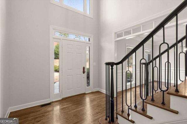 foyer with visible vents, a towering ceiling, stairway, wood finished floors, and baseboards