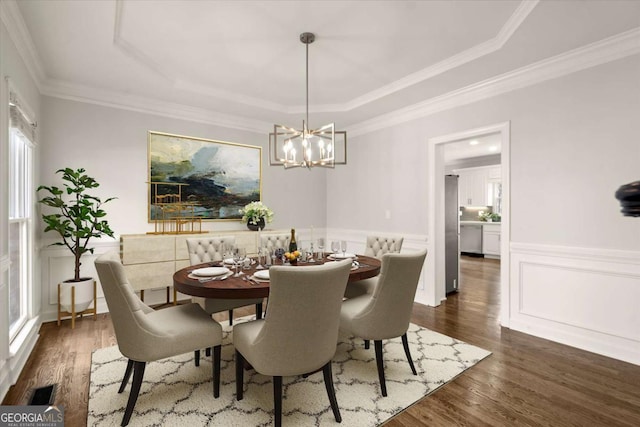 dining room featuring ornamental molding, dark wood-type flooring, wainscoting, and a raised ceiling