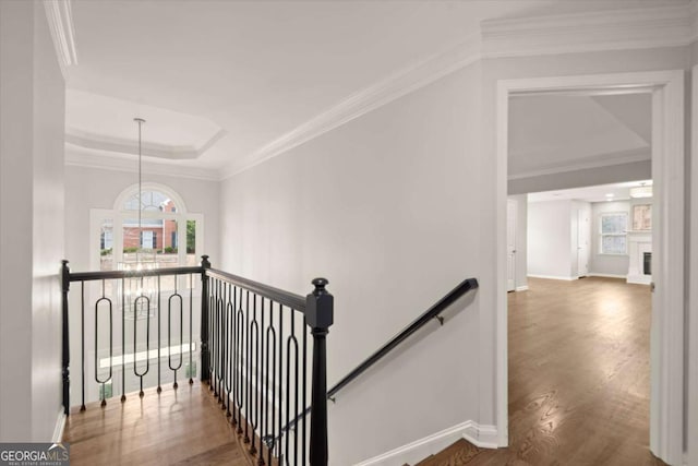 stairs featuring a fireplace, wood finished floors, baseboards, a raised ceiling, and crown molding