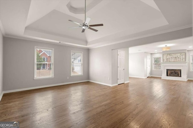 unfurnished living room with a raised ceiling, wood finished floors, and a glass covered fireplace