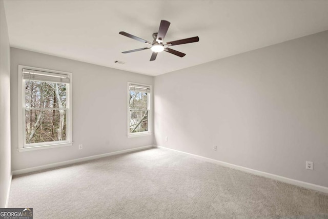 carpeted spare room with visible vents, baseboards, and ceiling fan