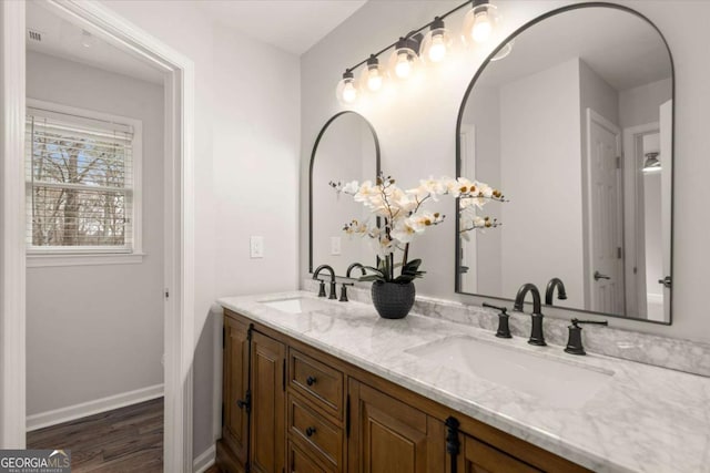 full bath featuring double vanity, wood finished floors, a sink, and baseboards