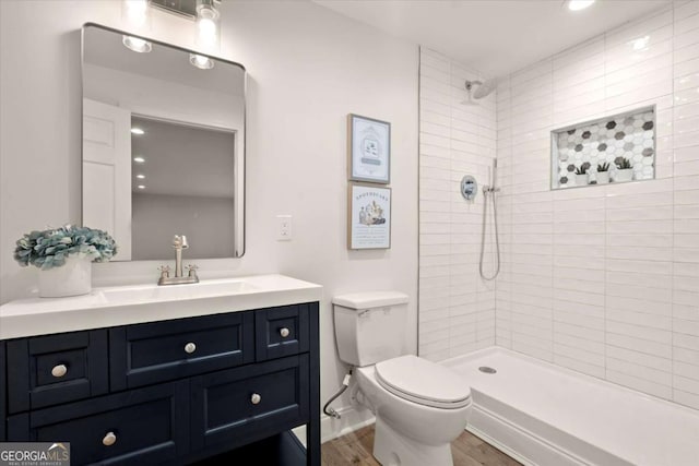 full bathroom featuring wood finished floors, tiled shower, vanity, and toilet