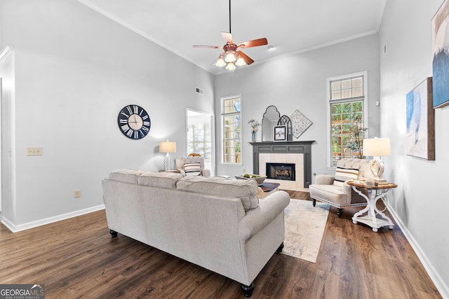 living room featuring baseboards, a tiled fireplace, ceiling fan, dark wood-type flooring, and crown molding