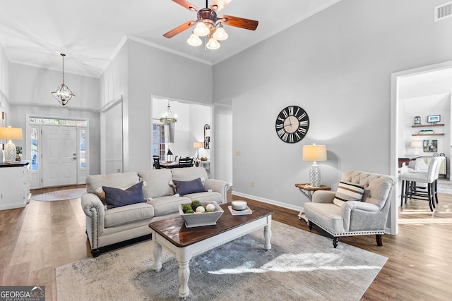 living room featuring baseboards, visible vents, ornamental molding, wood finished floors, and a high ceiling