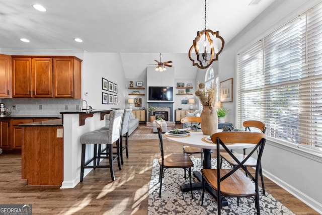 dining space with baseboards, wood finished floors, ceiling fan with notable chandelier, a fireplace, and recessed lighting