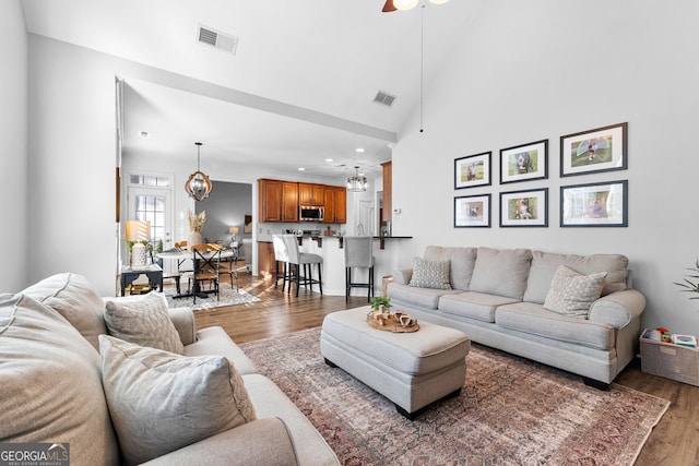 living area with high vaulted ceiling, a ceiling fan, visible vents, and wood finished floors