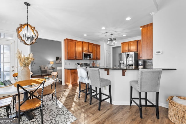 kitchen with dark wood-type flooring, appliances with stainless steel finishes, brown cabinetry, and an inviting chandelier