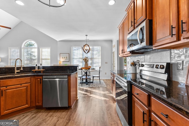 kitchen featuring tasteful backsplash, appliances with stainless steel finishes, brown cabinets, wood finished floors, and a sink