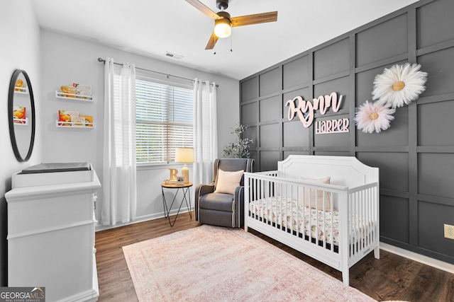 bedroom featuring visible vents, a decorative wall, an accent wall, wood finished floors, and a nursery area