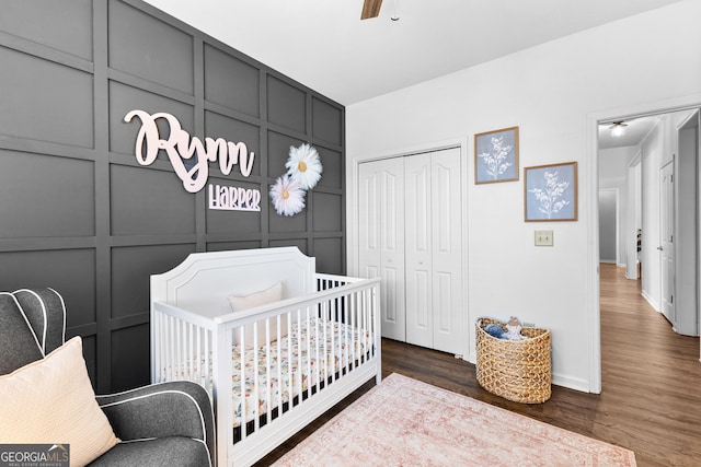 bedroom featuring a crib, dark wood-style flooring, a decorative wall, and a closet