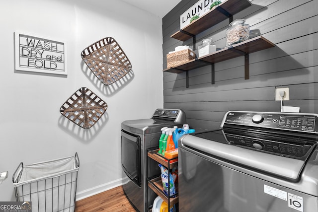 laundry area featuring laundry area, wood walls, wood finished floors, baseboards, and washer and clothes dryer