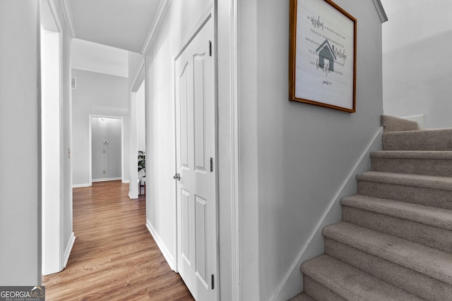 hallway featuring baseboards, crown molding, stairway, and light wood-style floors