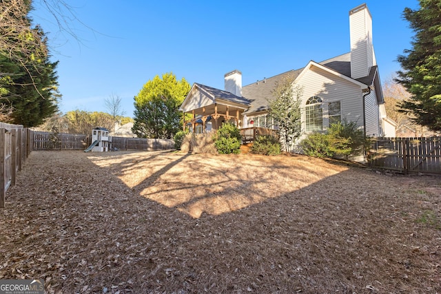 rear view of house featuring a fenced backyard, a playground, and a chimney