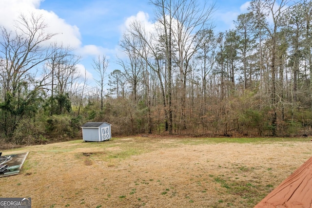 view of yard featuring an outbuilding, a view of trees, and a storage shed