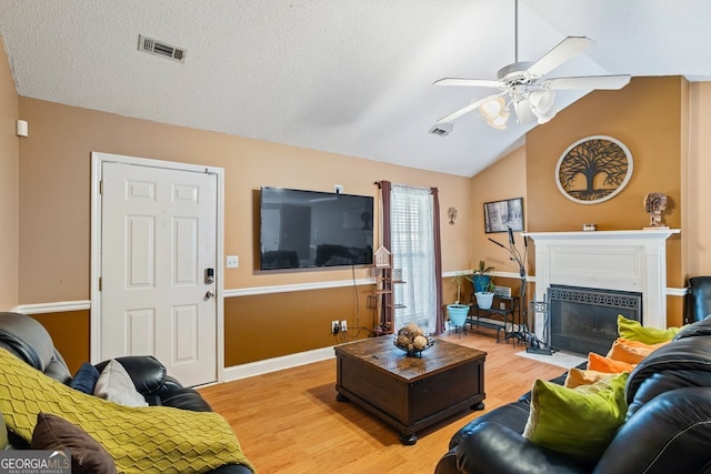 living room featuring a textured ceiling, light wood-style flooring, a fireplace with flush hearth, visible vents, and vaulted ceiling