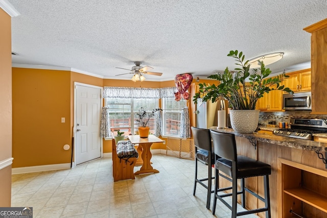 kitchen with crown molding, stainless steel appliances, tasteful backsplash, a ceiling fan, and a kitchen breakfast bar