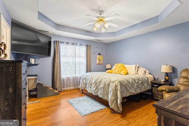 bedroom featuring a textured ceiling, ceiling fan, wood finished floors, and a raised ceiling