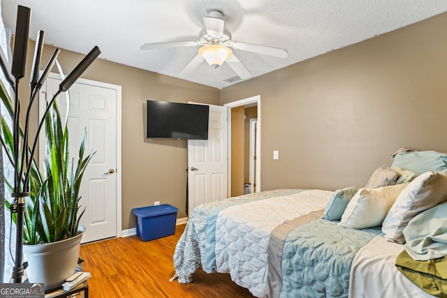 bedroom featuring light wood-style flooring, baseboards, ceiling fan, and a textured ceiling