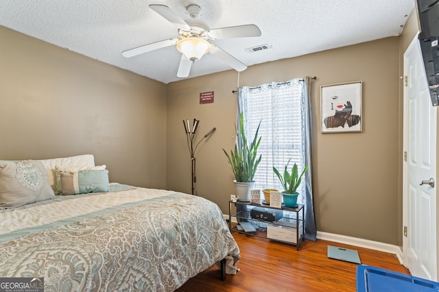 bedroom with a textured ceiling, wood finished floors, a ceiling fan, visible vents, and baseboards