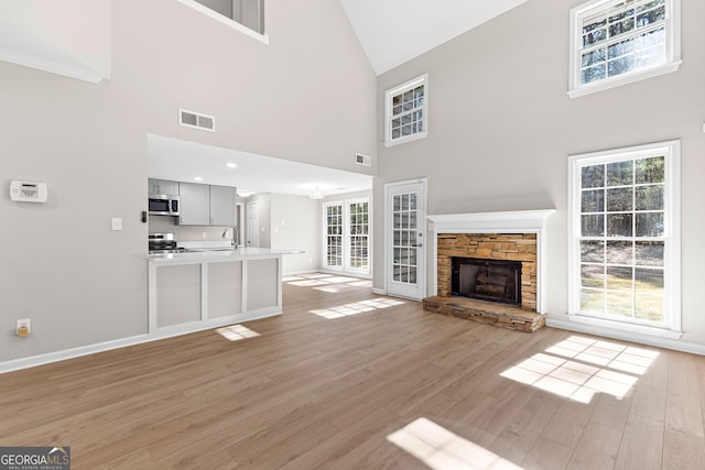 unfurnished living room featuring a stone fireplace, visible vents, light wood-style flooring, and baseboards