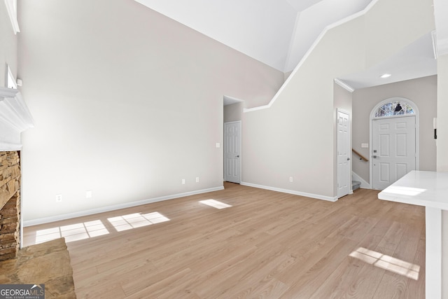 unfurnished living room featuring light wood-style floors, baseboards, a fireplace, and high vaulted ceiling