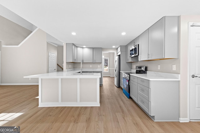 kitchen featuring stainless steel appliances, light countertops, gray cabinetry, light wood-type flooring, and a peninsula