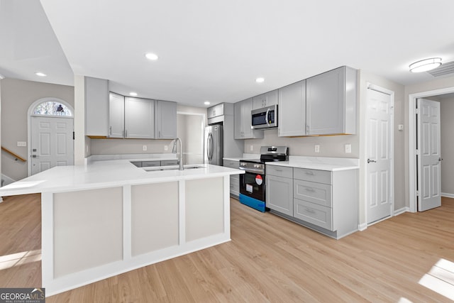 kitchen featuring a peninsula, gray cabinets, stainless steel appliances, and a sink