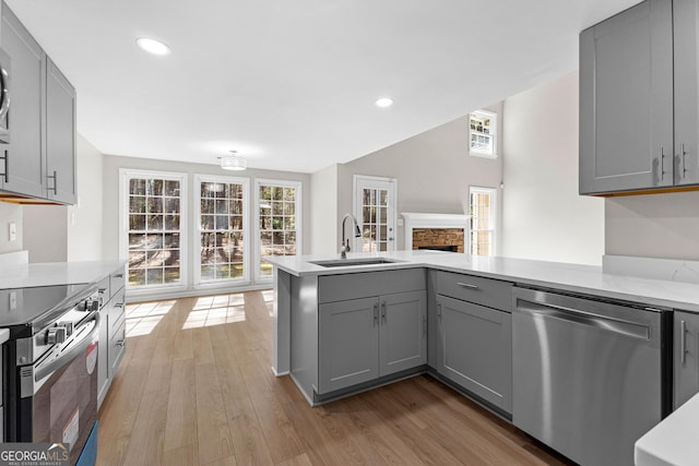 kitchen with wood finished floors, a peninsula, stainless steel appliances, gray cabinetry, and a sink