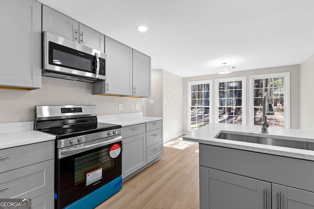 kitchen featuring light stone counters, light wood finished floors, gray cabinetry, appliances with stainless steel finishes, and a sink