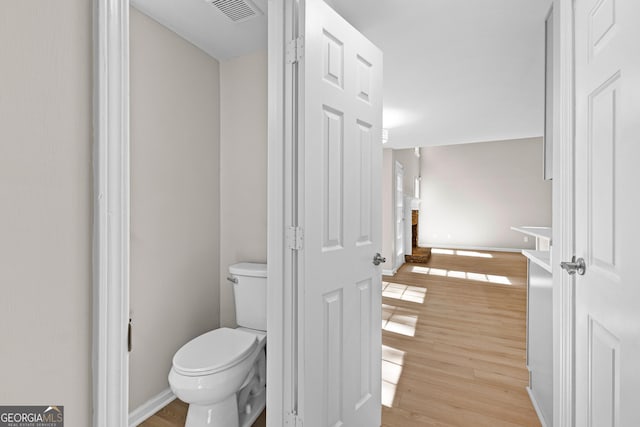 bathroom with baseboards, visible vents, toilet, and wood finished floors