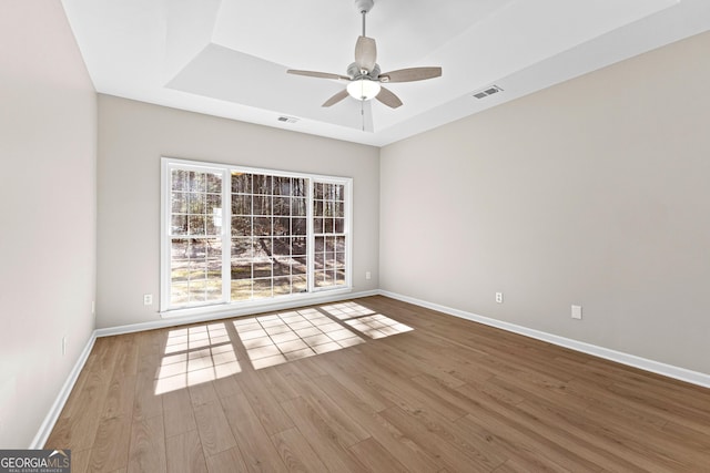 empty room with baseboards, visible vents, a tray ceiling, and wood finished floors