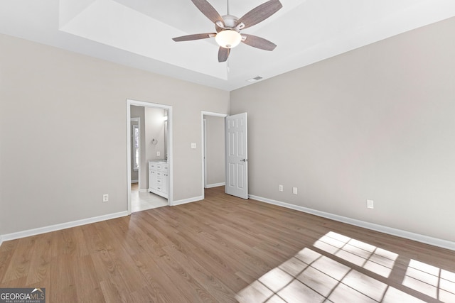 unfurnished bedroom featuring visible vents, baseboards, a raised ceiling, light wood finished floors, and ensuite bath